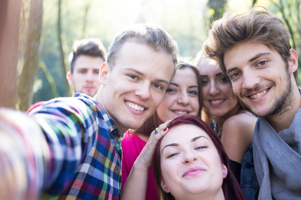 Young people having good time together in park on river and taking selfie